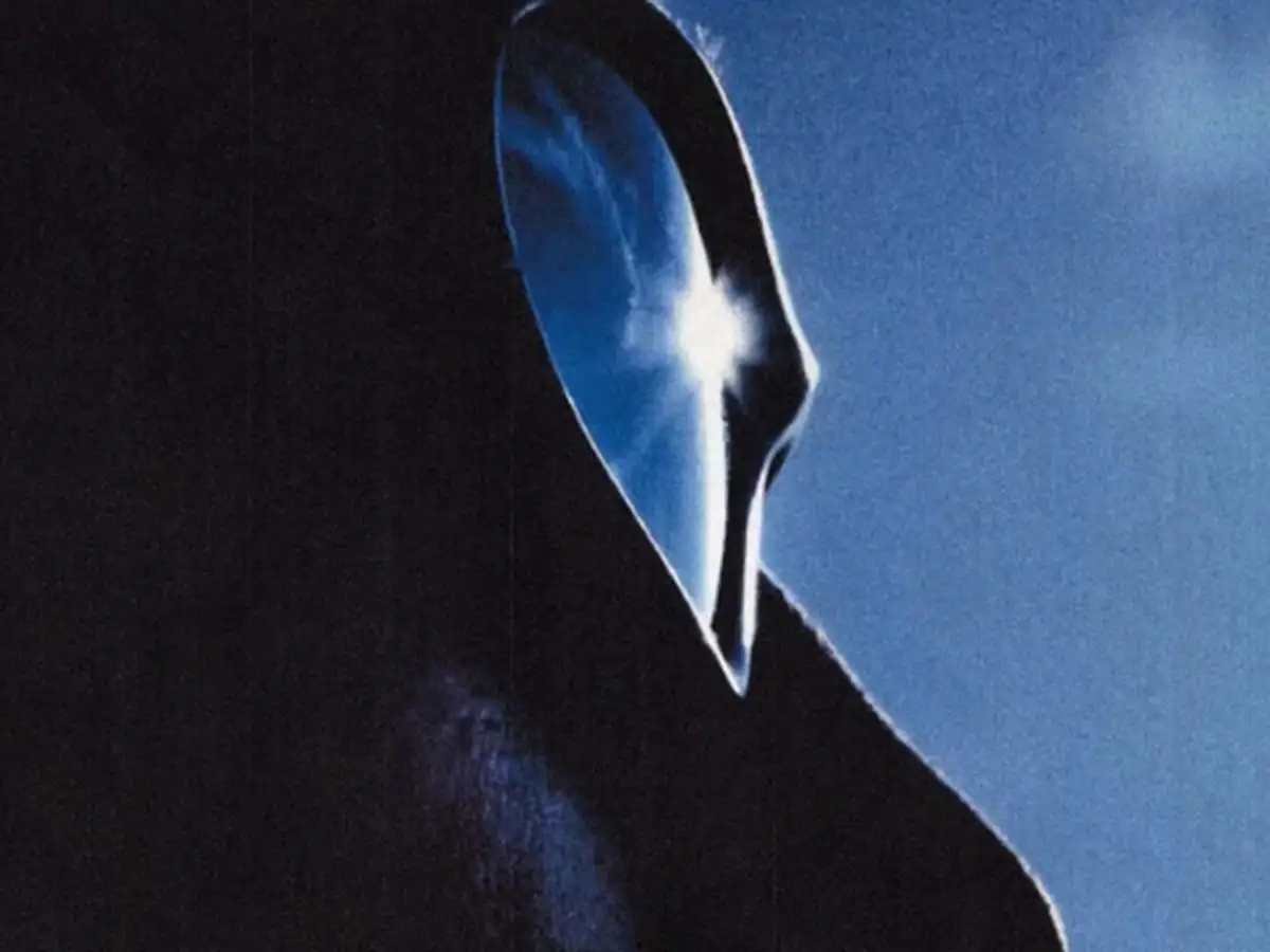 A face in silhouette against a deep blue sky, the sun reflected in dark glasses.